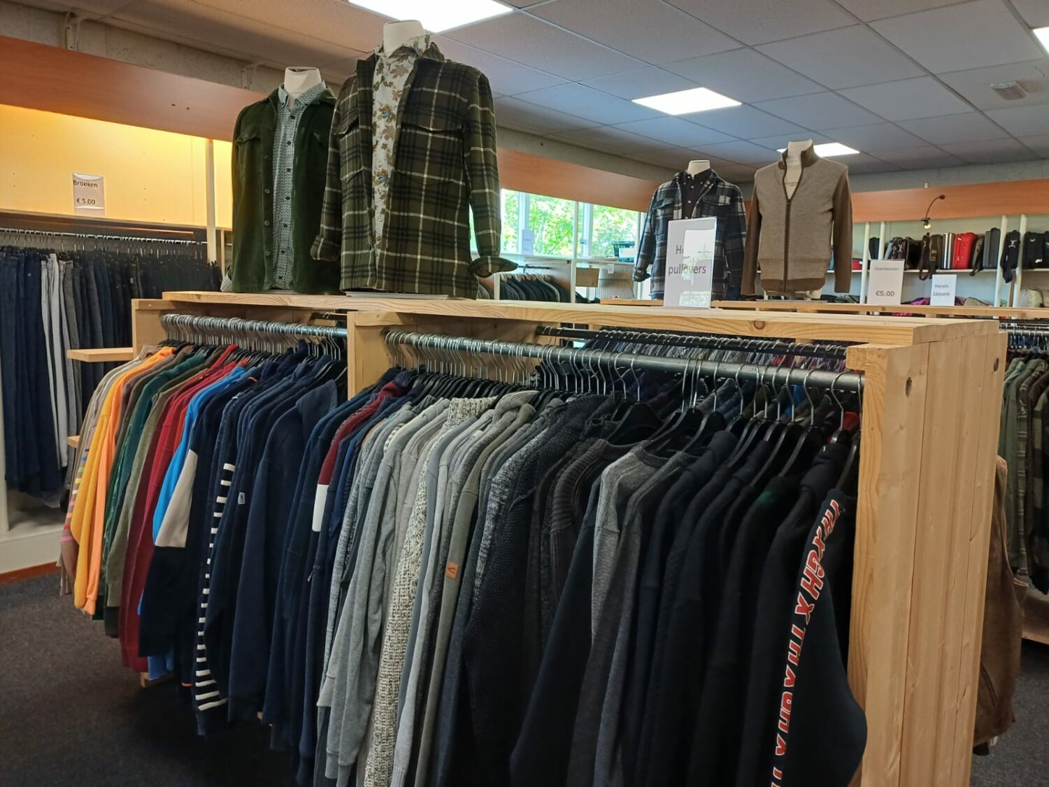 Kledingwinkel met diverse jassen en truien op hangers, gericht op humanitaire hulp en armoedebestrijding, passend bij de missie van Dorcas.