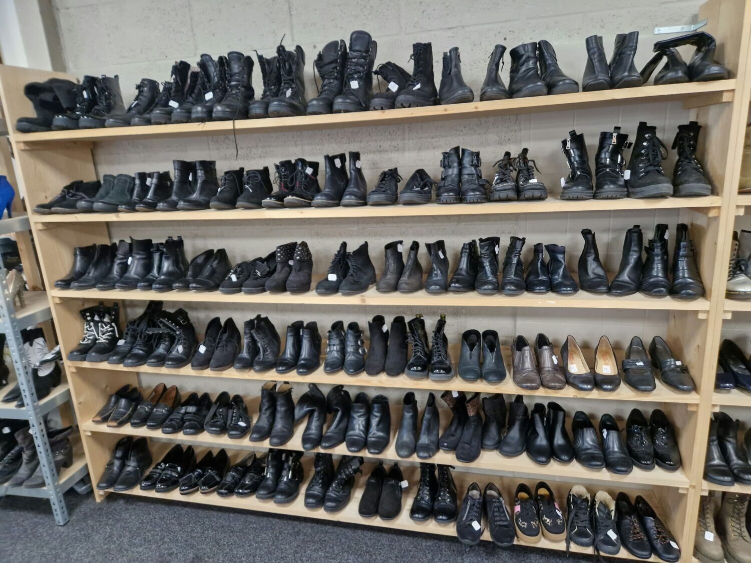 Grote collectie zwarte schoenen en boots op houten schoenenrek, geschikt voor humanitaire hulp en noodhulpprojecten in Oost-Europa, Oost-Afrika en het Midden-Oosten.