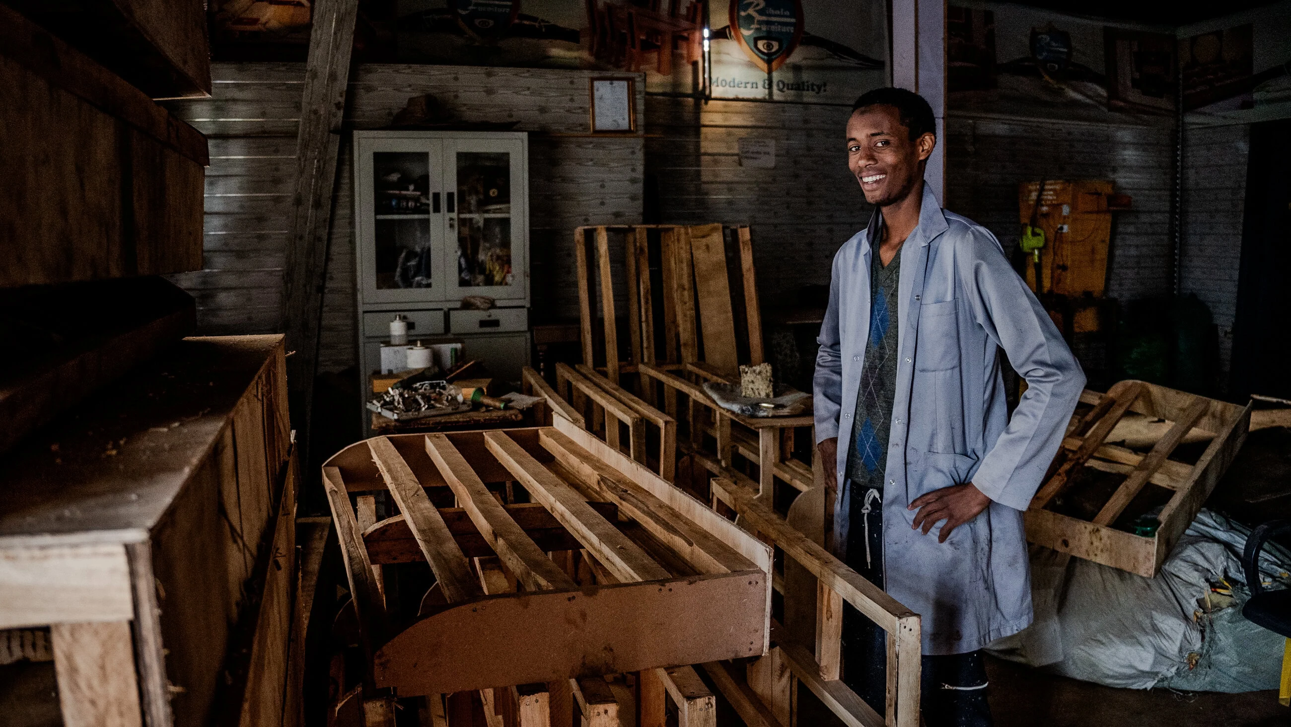 Een jonge man in een werkplaats met houten pallets en gereedschap, symboliseert humanitaire hulp en armoedebestrijding in ontwikkelingslanden, passend bij Dorcas' missie.