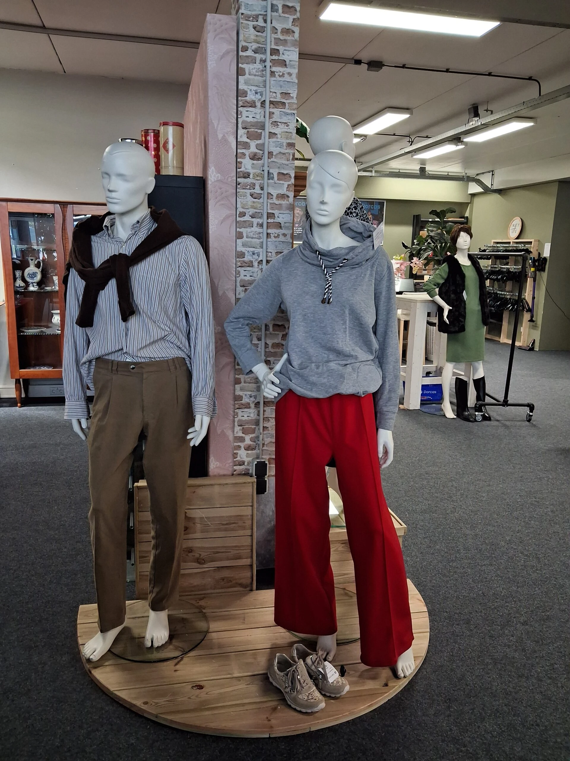 Twee mannequins in een winkel, gekleed in casual kleding, met een achtergrond van winkelrekken en een klant die winkelt, symboliseert mode en retail. Geschikt voor een overzicht van winkelpresentatie.