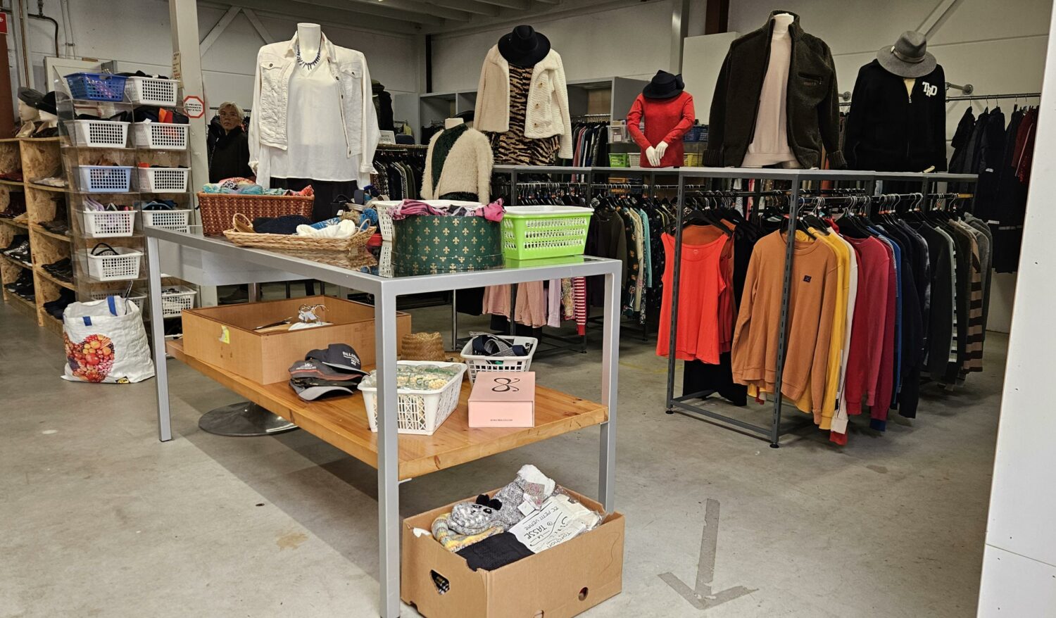 Inrichting van een kledingwinkel met diverse kledingstukken en accessoires, gericht op het ondersteunen van mensen in armoede en noodhulp, passend bij de missie van Dorcas.