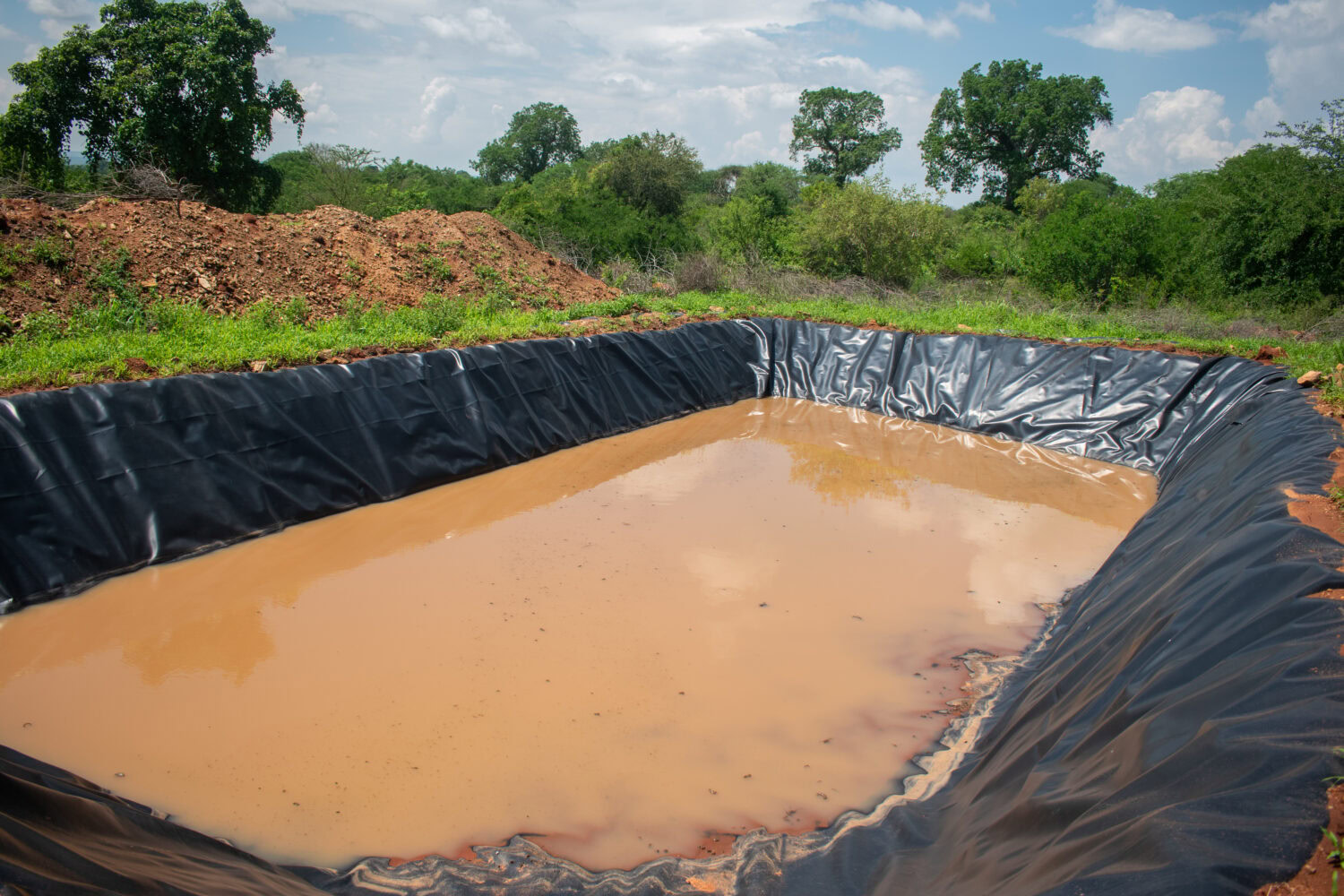 Een grote wateropvangbak met bruin water, omgeven door groen landschap en bomen, gebruikt voor irrigatie en waterbeheer in ontwikkelingsgebieden.