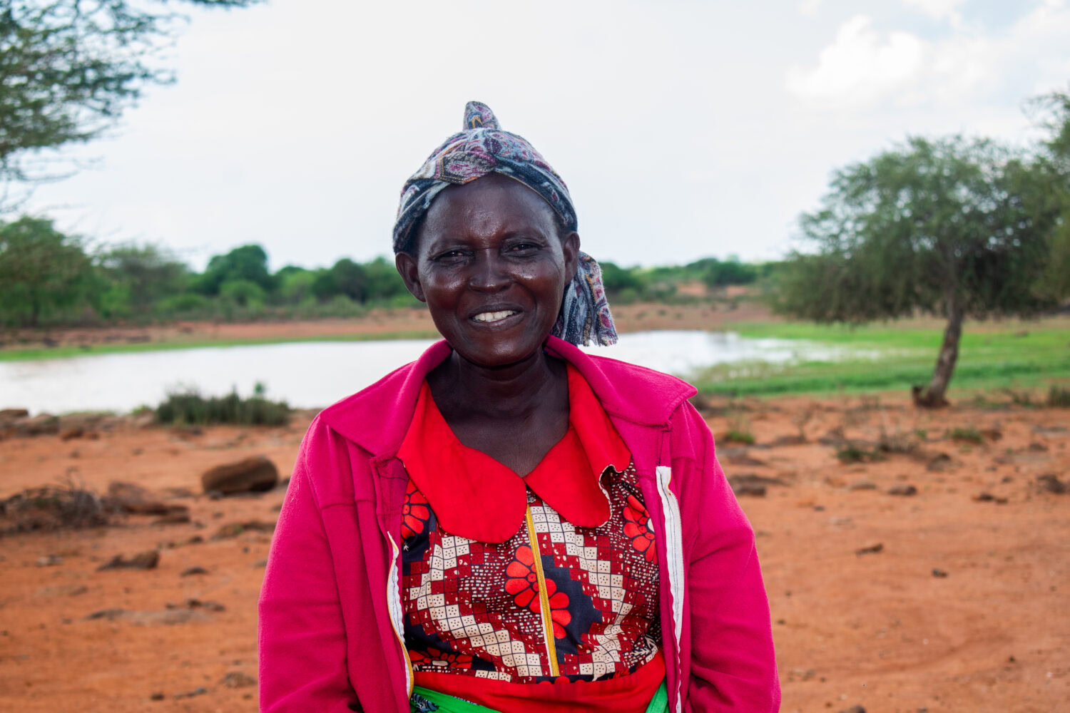 Vrolijke vrouw in kleurrijke kleding met bijen in Oost-Afrika, symboliseert hulp en hoop in humanitaire projecten van Dorcas.