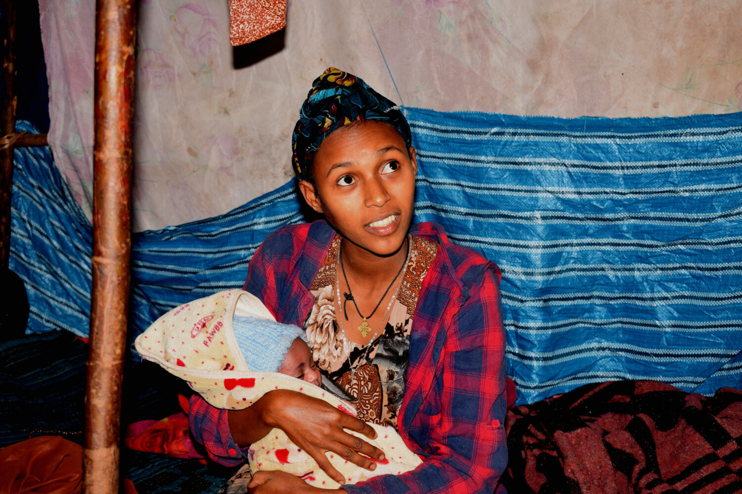 Moeder houdt baby dicht tegen zich in een eenvoudige kamer met kleedjes en dekens, dorcas-impact in noodhulp en armoedebestrijding.