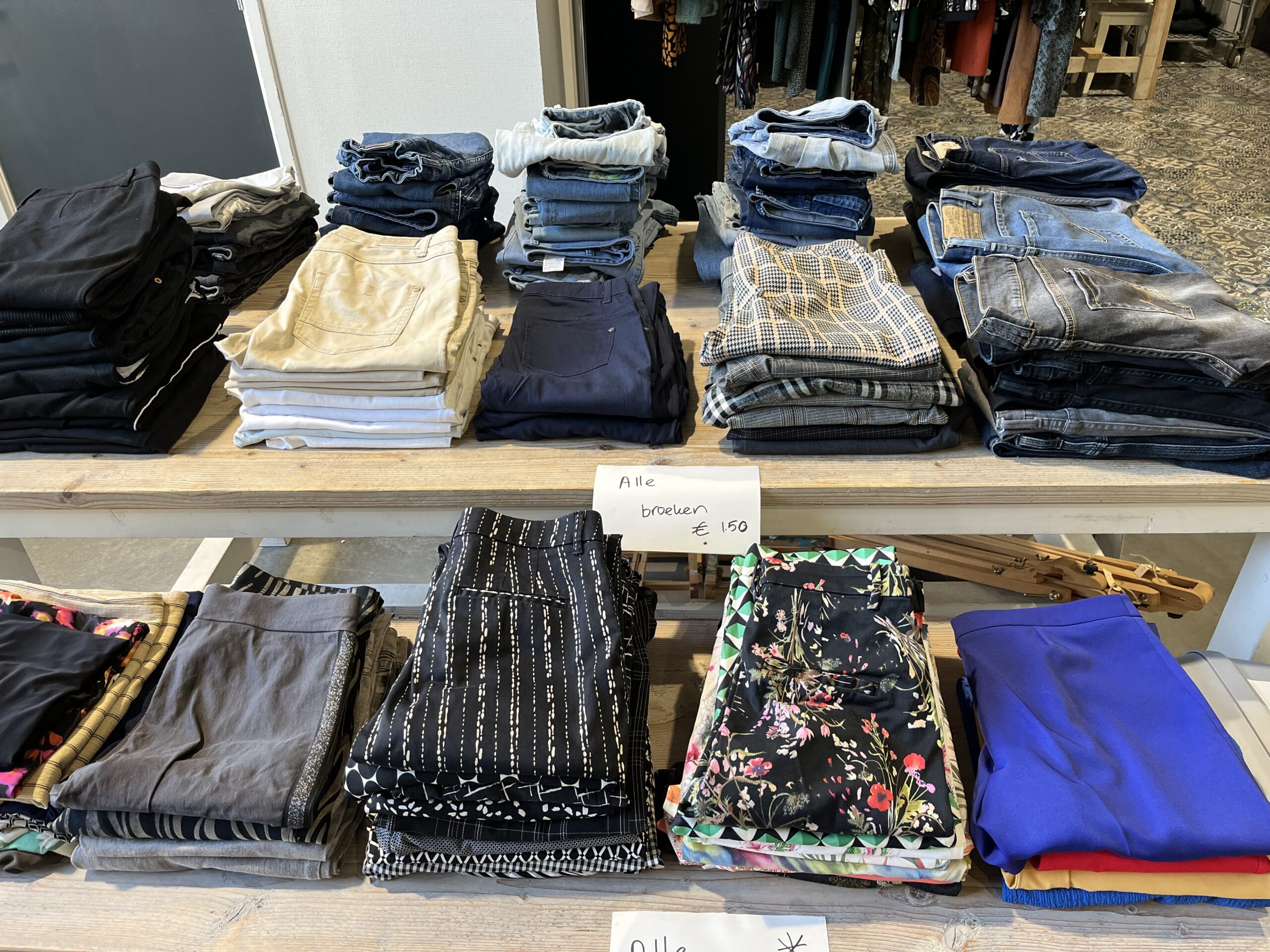 Verschillende gestapelde kledingstukken zoals jeans, broeken en shirts in een winkel, symboliseert hulp en armoedebestrijding door Dorcas in ontwikkelingslanden.
