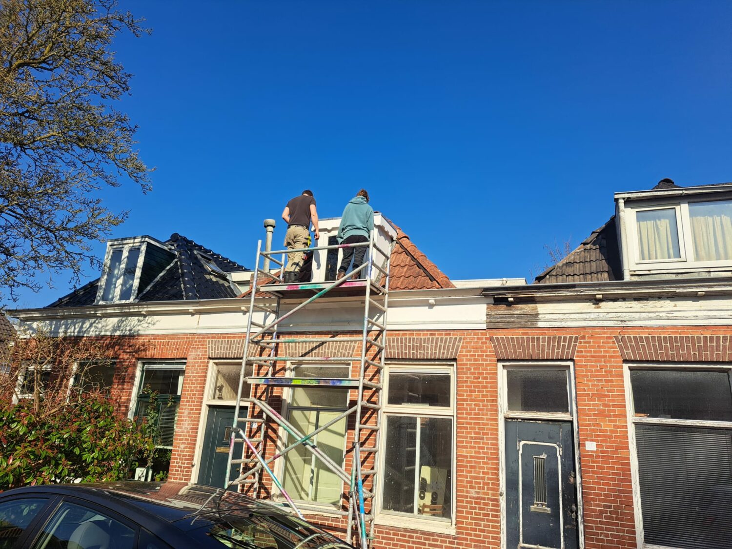 Twee arbeiders op een steiger repareren het dak van een traditioneel Nederlands huis, symboliseert bouw en herstel, passend bij humanitaire hulp en armoedebestrijding in ontwikkelingslanden.