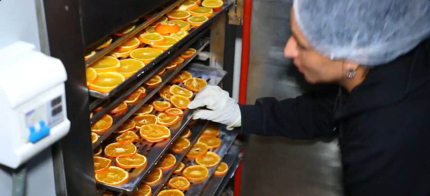 Werknemer controleert en verwerkt gedroogde sinaasappelschijfjes uit een warme oven, als onderdeel van noodhulpporrt.