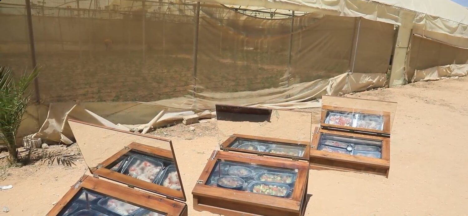 Draagbare zonnekoelboxen of koelvoorzieningen opgesteld op zandgrond, klaar voor distributie als noodhulp in een veldkamp van Dorcas.
