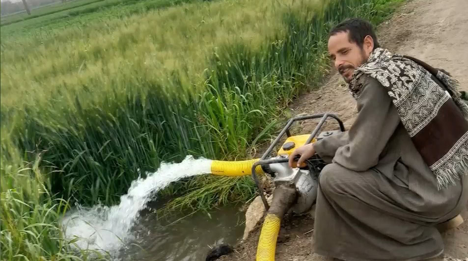 Man bij een waterkraan in een groen veld, dorpsweg, handmatig leidingwater tappend; duurzaam waterbeheer en menselijke waardigheid centraal in noodhulp en ontwikkeling door Dorcas.