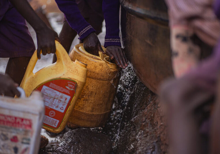 Een afbeelding van mensen die water uit een bron halen met behulp van een jerrycan en emmers, illustrerend duurzame watervoorziening en gemeenschapsinitiatieven.