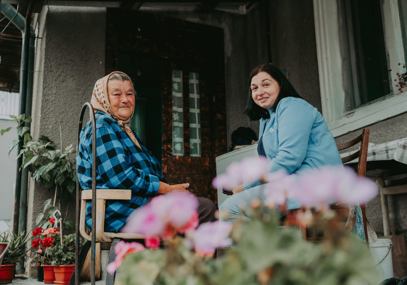 Oudere vrouw krijgt bezoek van jonge vrouw op haar veranda, samen lachen en praten.