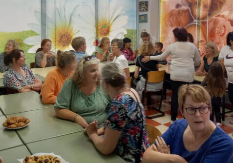 Baukje Krol Albanië vrouwenreis Gezellig bijeenkomst met mensen die in gesprek zijn, in een kleurrijke ruimte met muurdecoraties van bloemen en lachende kinderen, georganiseerd door Dorcas.