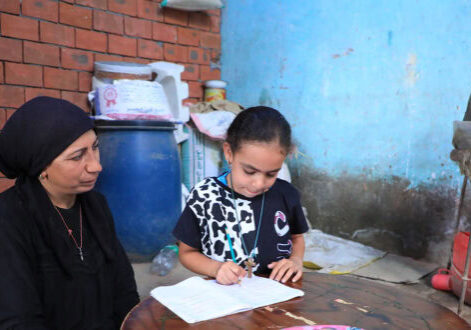 The mother is helping her daughter with her studies. 9-13-2025. Kind vrouw en meisje leren samen in een eenvoudige kamer met bakstenen muur en schoorsteen in een ontwikkelingsland.